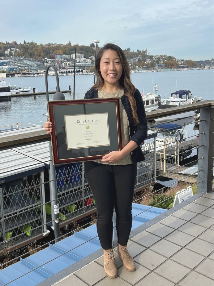 Dr. Erin Cho holding her framed Kois Center certificate by the water in Seattle
