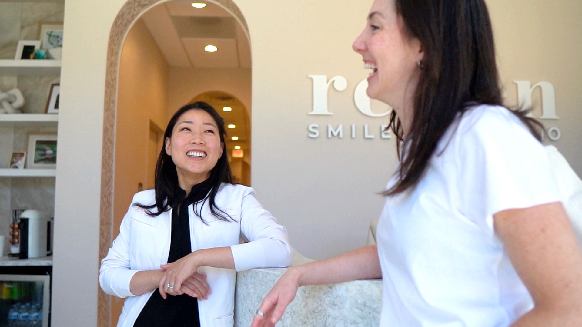 Dr. Erin Cho laughing with a patient at the reception desk of Re·gen Smile Studio