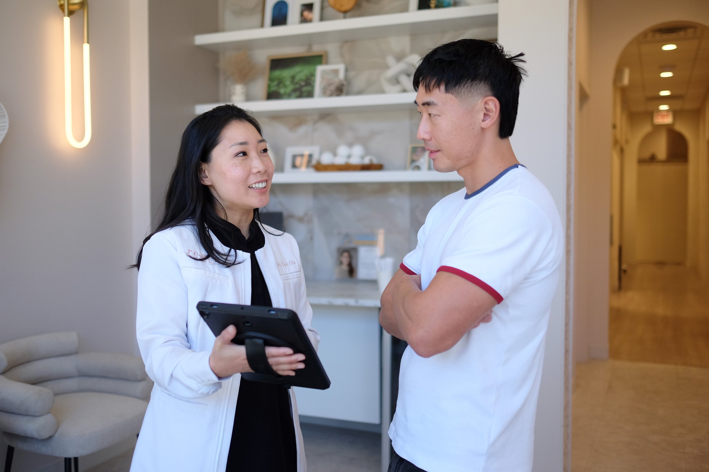 Dr. Erin Cho with a tablet, talking with a patient by the shelves