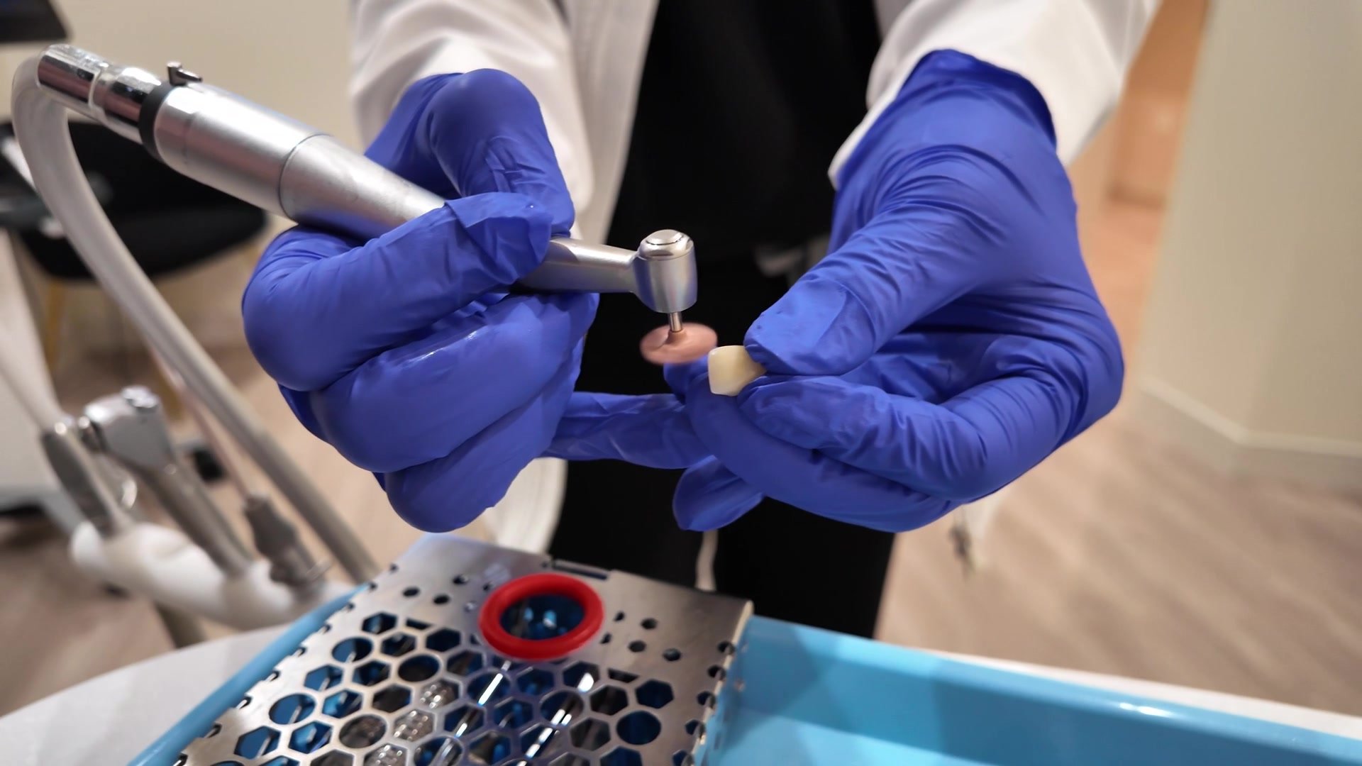 Gloved hands holding a dental handpiece over an instrument tray
