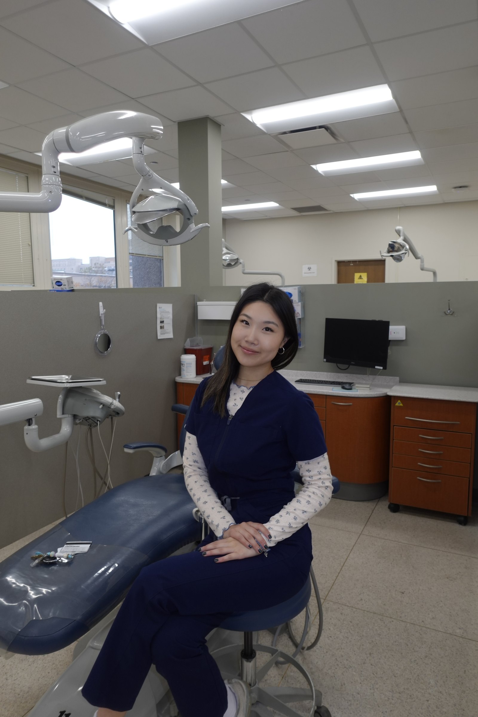 Dr. Ashley Choi seated in a dental operatory in navy scrubs